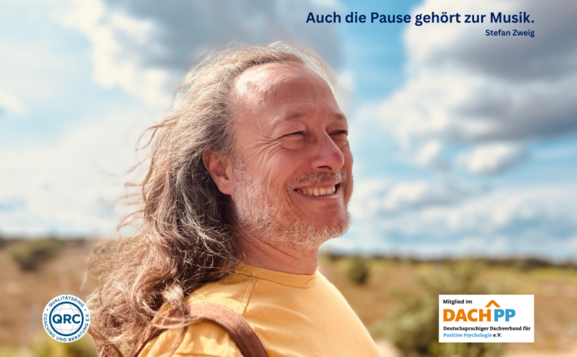 Foto von Torben Klußmann. Links unten das Logi des QRC e.V, und rechts unten das Logo des DACH^PP e.V. Er steht seitlich mit Blick nach rechts und lächelt. Den Hintergrund stellt mehr als die Hälfte ein Himmel mit Blau zwichen weißen und grauen Wolken. Die untere Hälfte des Hintergrunds zweigt eine Heidelandschaft. Er lächelt. Rechts über dem Kopf steht Auch die Pause gehört zur Musik. Stefan Zweig
